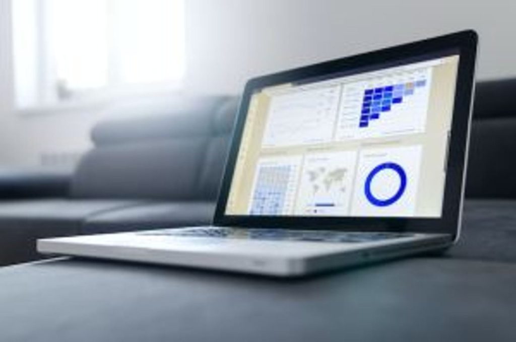 A laptop computer with charts on the screen sits on an office couch.